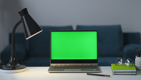 person-is-switching-off-lamps-and-laptop-in-room-at-evening-finished-working-green-screen-on-notebook-for-chroma-key-technology-closeup-on-table-surface